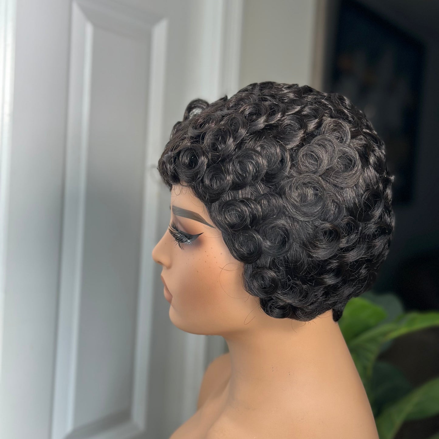 Mannequin head with curly black hair against a neutral background
